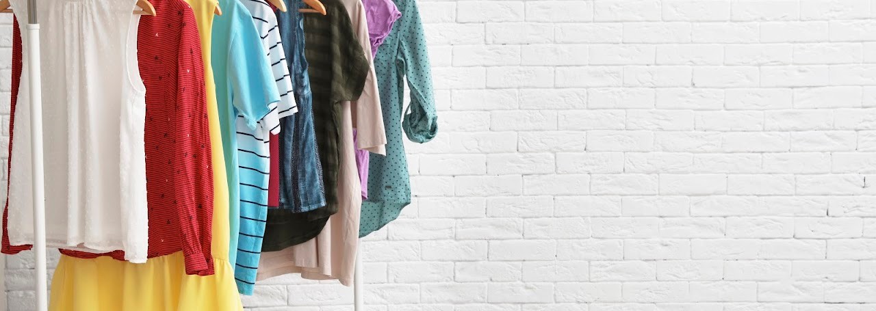 Wardrobe rack with stylish clothes and shoes near brick wall indoors. Space for text